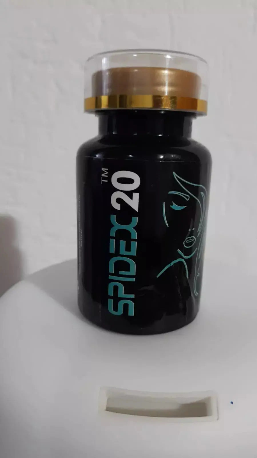 Black bottle of SPIDEX 20 herbal supplement with gold and transparent cap, minimalist face line art
